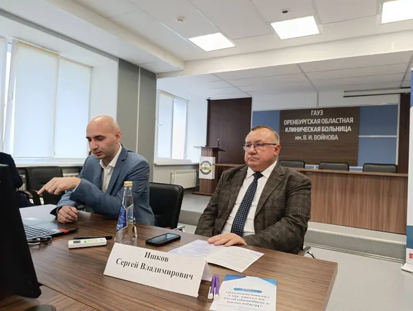 Двое участников за столом на фоне вывески областной клинической больницы