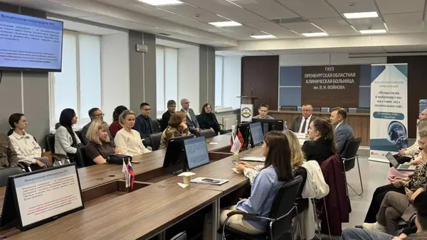 Ряды слушателей за длинными столами, справа баннер конференции