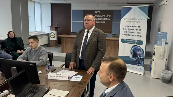 Модератор стоя обращается к залу рядом с баннером конференции
