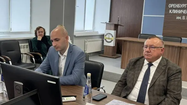 Двое за рабочим столом: один готовит доклад на ноутбуке, второй слушает