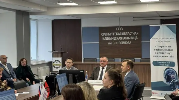 Актовый зал с вывеской больницы и баннером конференции, участники за столами