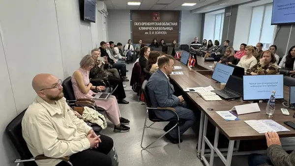 Слушатели вдоль столов зала, на переднем плане врач в светлой куртке