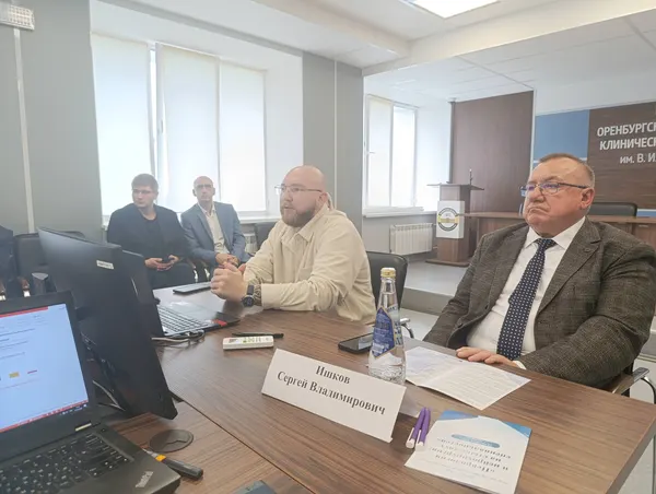 Участник в светлом пиджаке слушает выступление за столом в зале